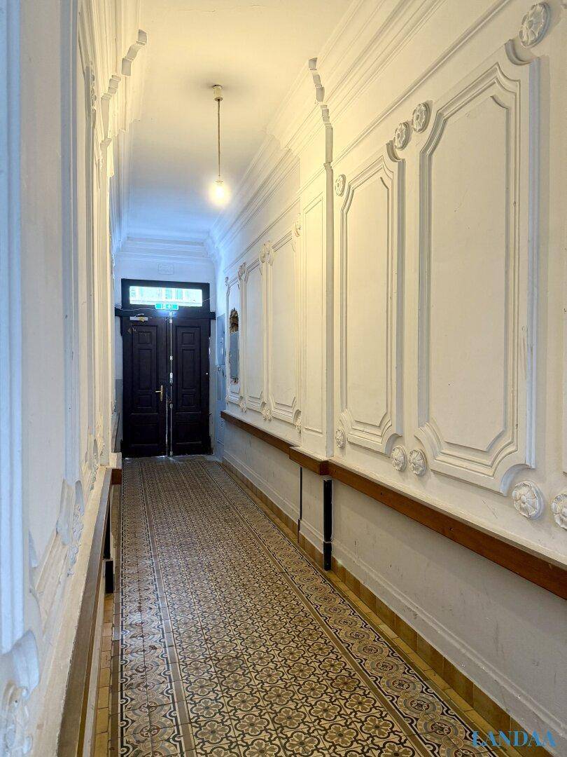 Langer Flur mit Stuckverzierungen an den Wänden und einem gemusterten Fliesenboden.