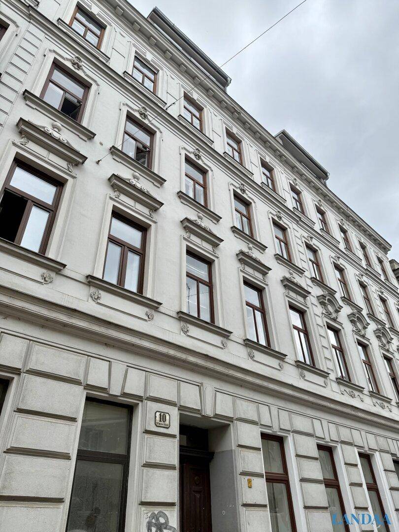 Historische Fassade eines Mehrfamilienhauses mit vielen Fenstern und dekorativen Elementen.