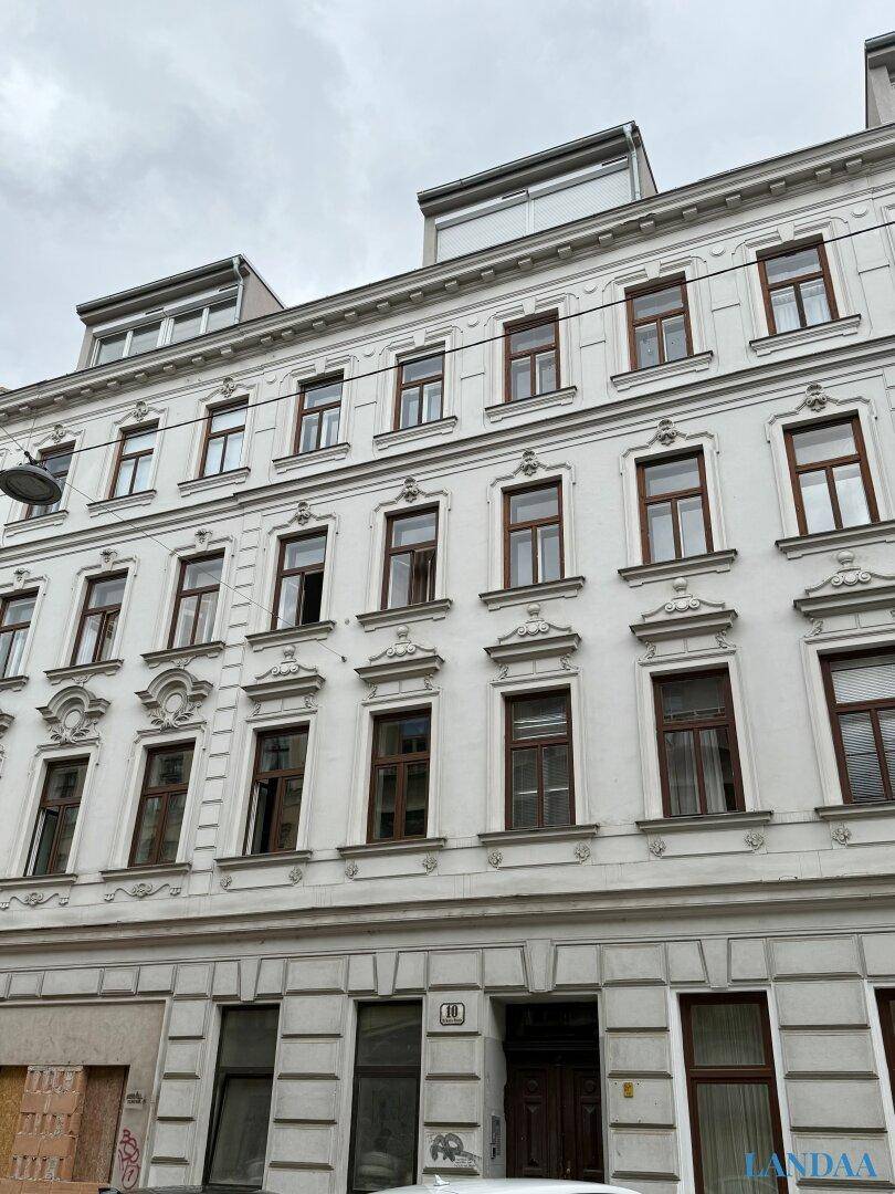 Ansicht der weißen Fassade eines Altbaus mit zahlreichen Fenstern und einem Dachaufbau.