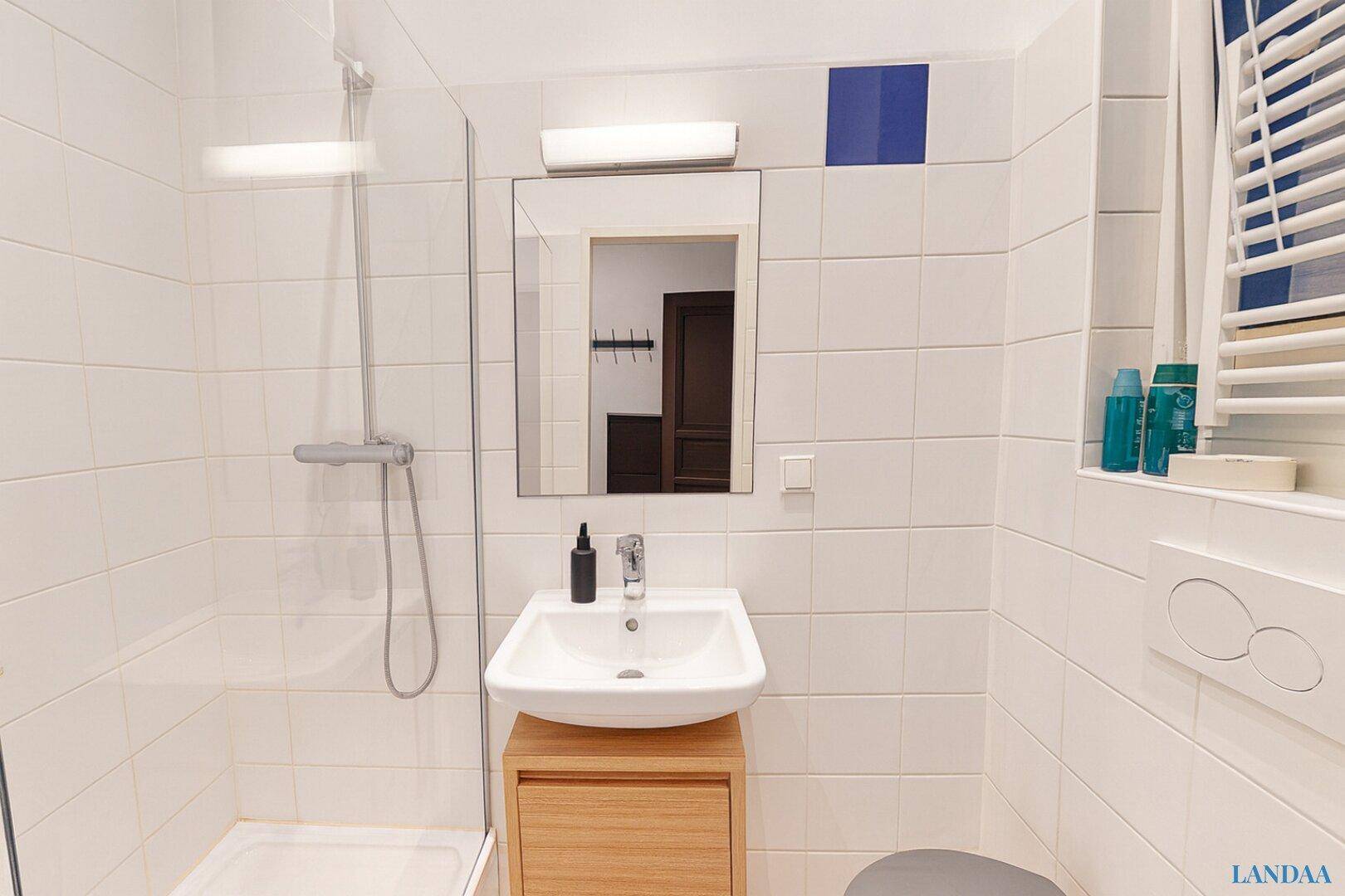 Modernes Badezimmer mit weiß gefliesten Wänden, Dusche und Waschbecken mit Holzunterschrank.