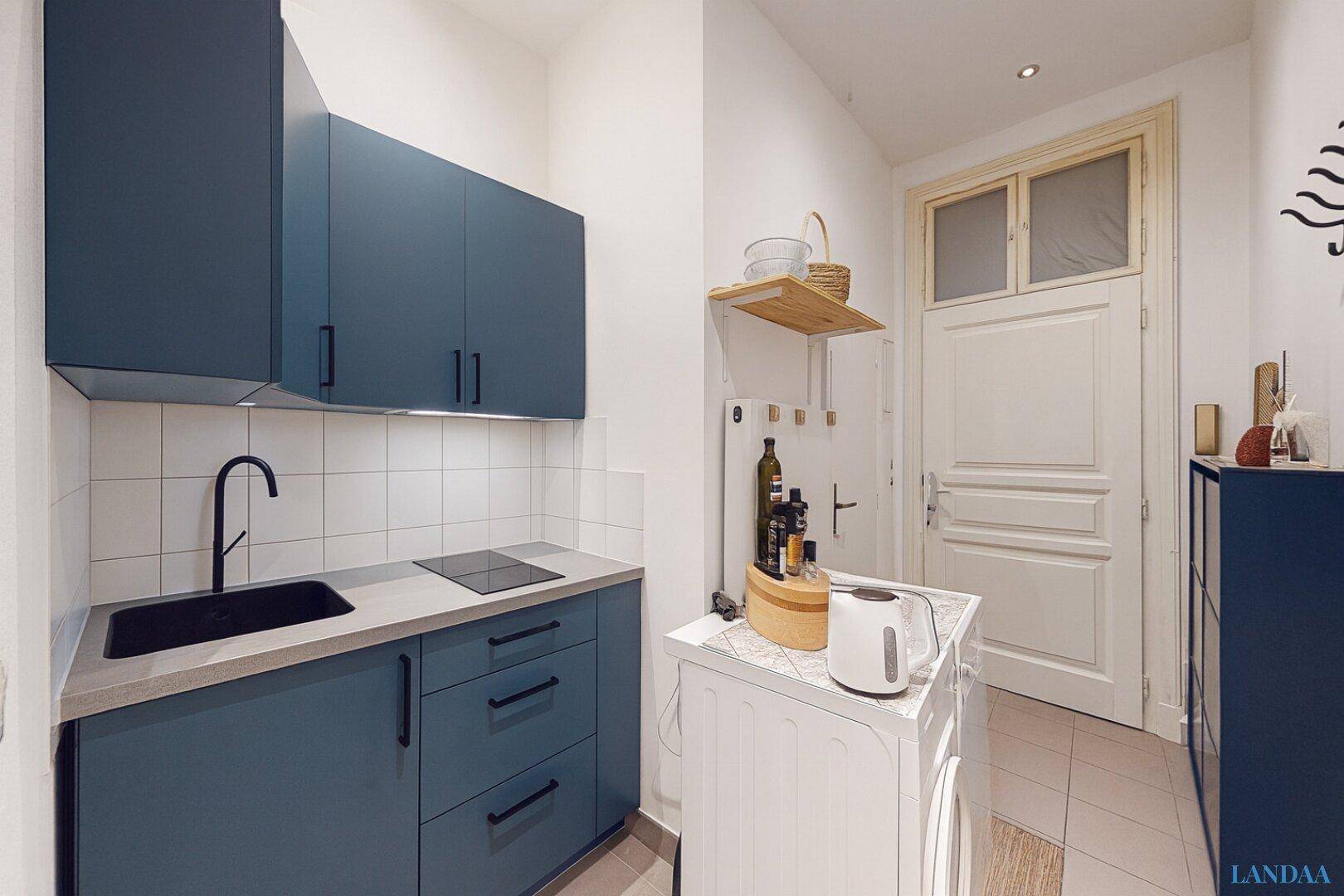 Kleine, moderne Küche mit blauen Schränken, Induktionskochfeld und integrierter Waschmaschine.