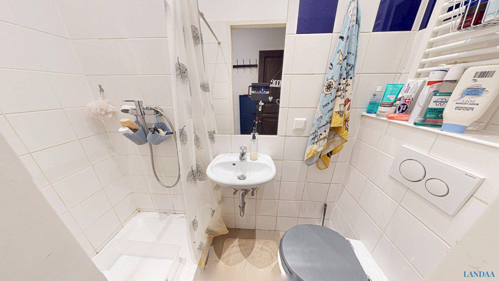 Funktionales Badezimmer mit Duschbereich, WC und Waschbecken, komplett weiß gefliest.