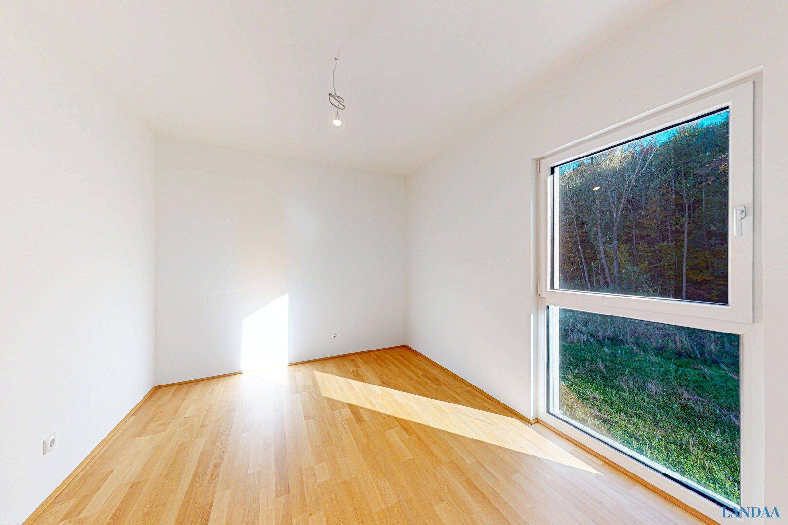 Sonniges, unmöbliertes Zimmer mit Holzboden und weitem Blick ins Grüne.