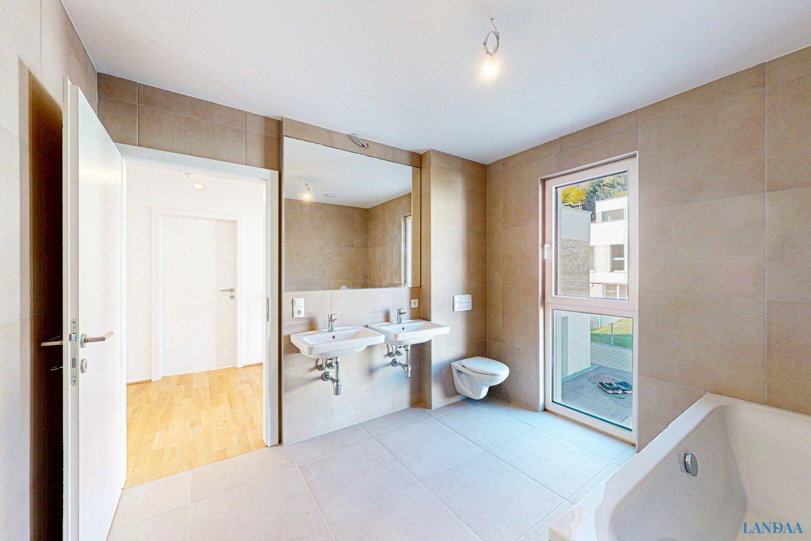 Modernes Badezimmer mit beigen Fliesen, Doppelwaschbecken, Toilette und Fenster.