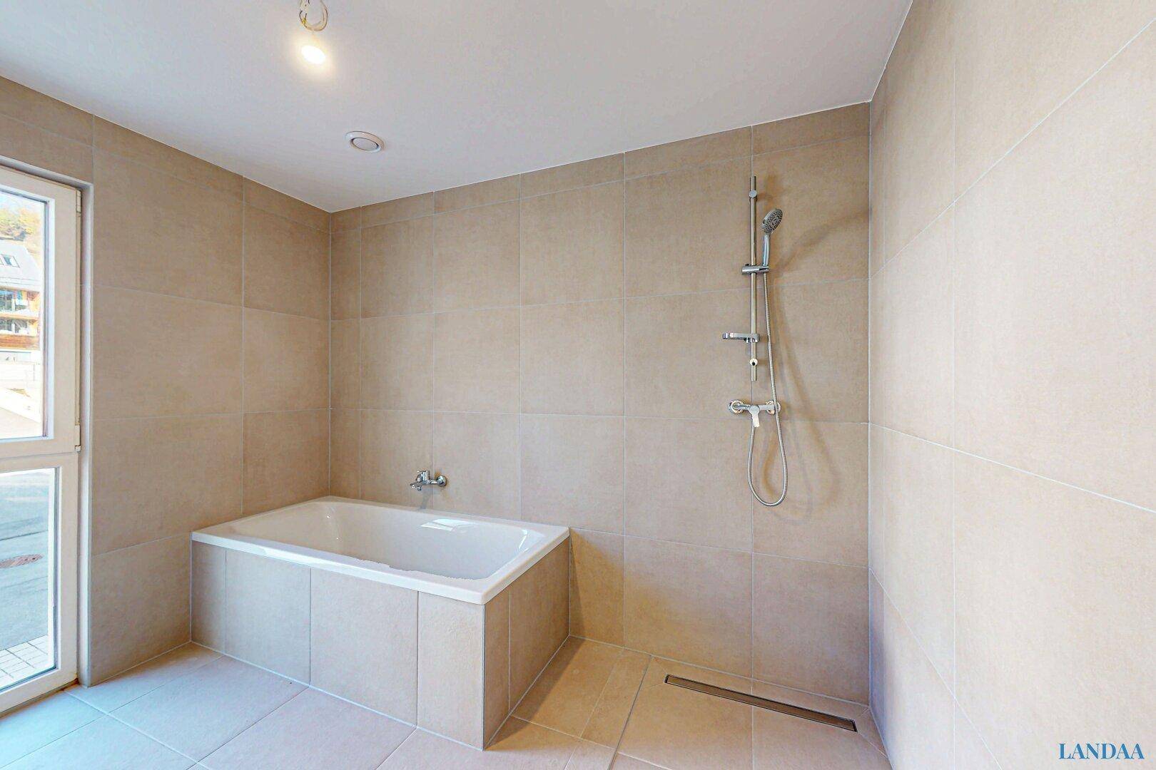 Geräumiges Badezimmer mit eingebauter Badewanne und Duschbereich, komplett gefliest.