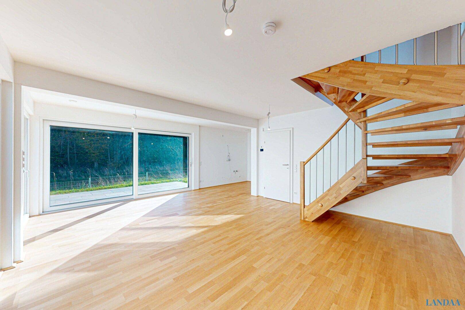 Heller Wohnbereich mit Holzboden, großen Fenstern und einer eleganten Holztreppe.