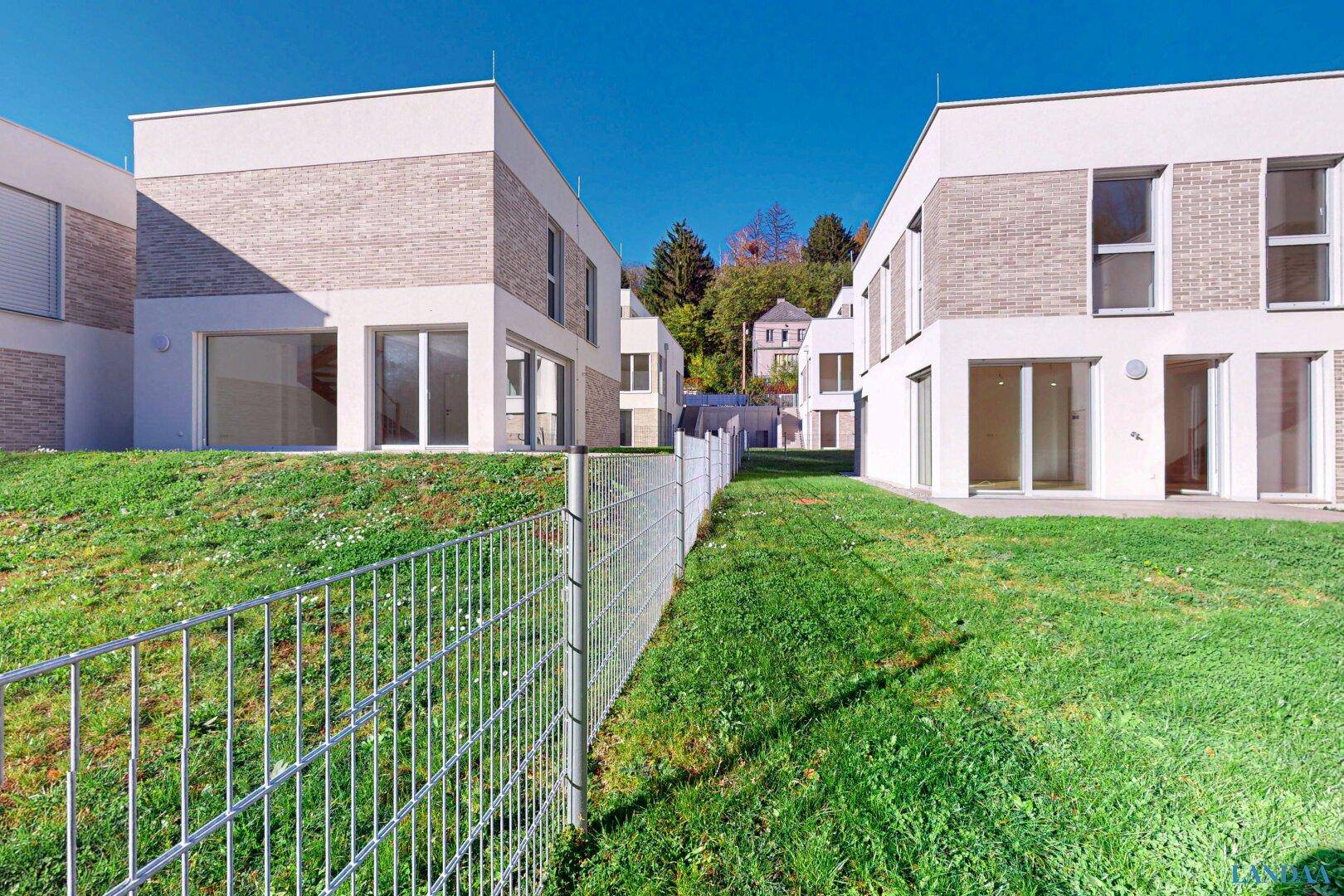 Moderne Reihenhäuser mit weißer Fassade und Ziegelakzenten, umgeben von grünen Rasenflächen.