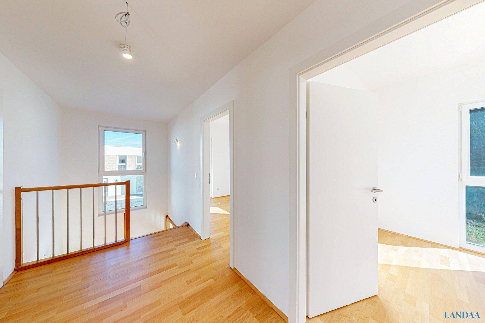 Heller Flur mit Holzgeländer und Parkettboden, der zu weiteren Räumen und einer Treppe führt.
