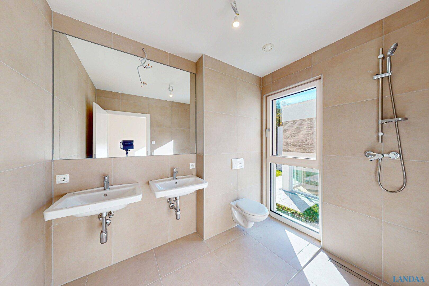 Modernes Badezimmer mit beigefarbenen Fliesen, Doppelwaschbecken, wandhängendem WC und Dusche.
