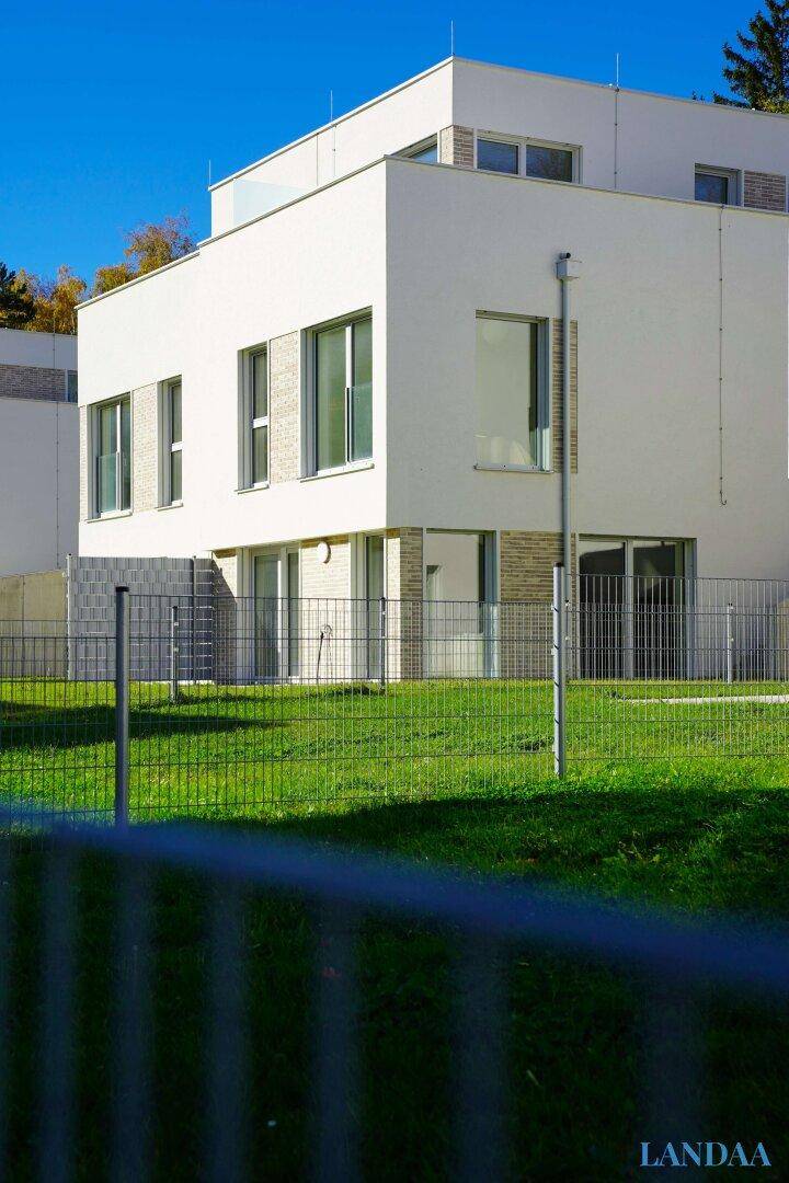 Moderne Gebäudefassade mit großen Fenstern und einem gepflegten Rasen im Vordergrund.