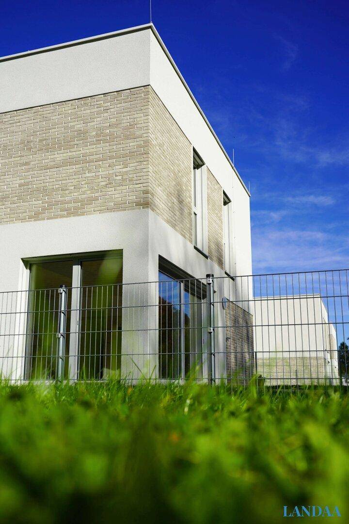 Moderne Hausfassade mit hellen Ziegeln und großen Fenstern unter blauem Himmel.