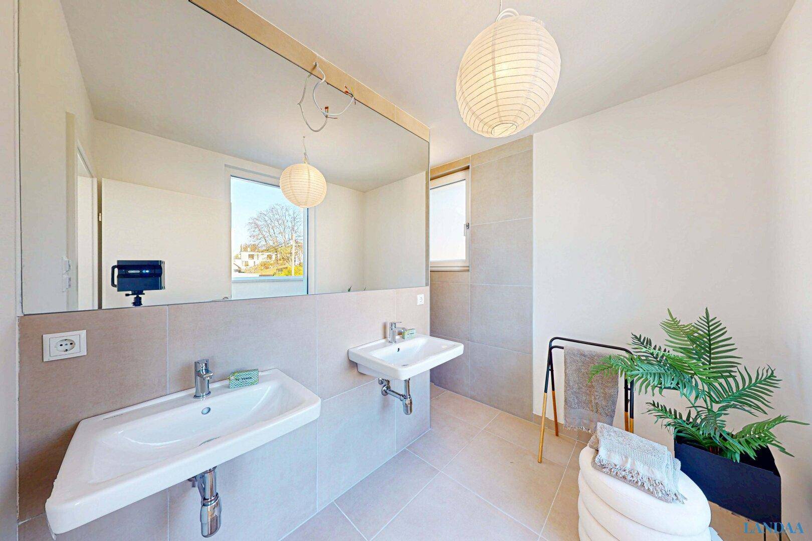 Modernes Badezimmer mit beigefarbenen Fliesen, zwei Waschbecken und großem Spiegel.