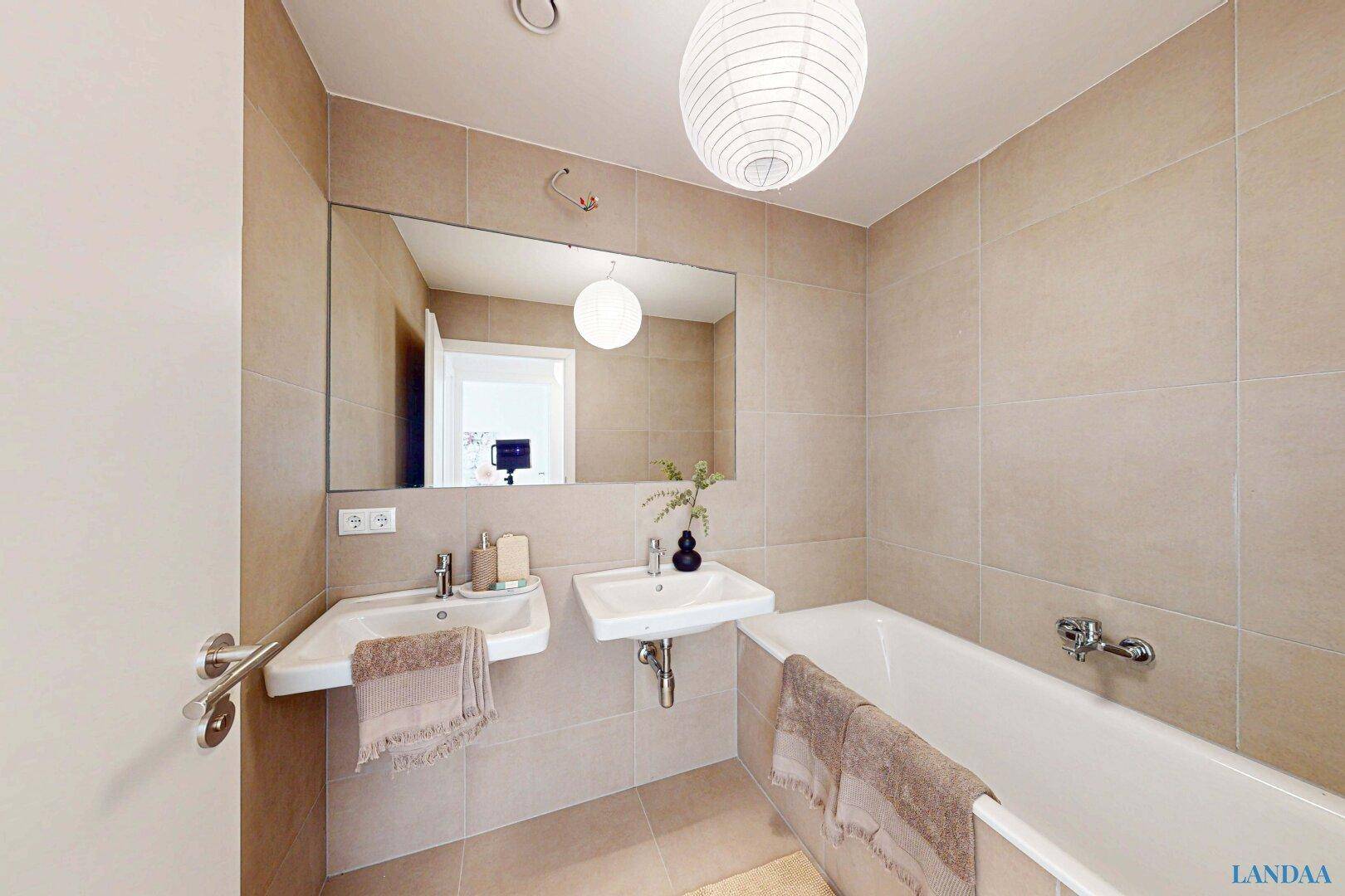 Modernes Badezimmer mit beigefarbenen Fliesen, Badewanne und Doppelwaschbecken.