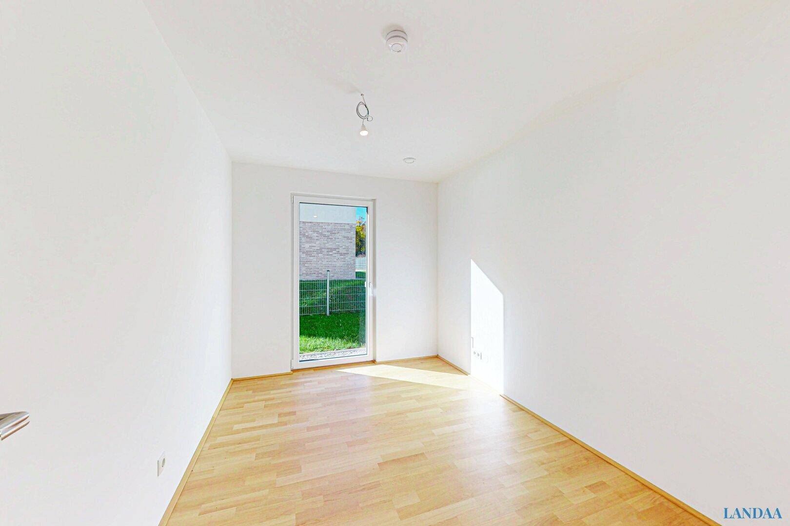 Helles Zimmer mit Holzparkettboden und direktem Zugang zur grünen Außenfläche.