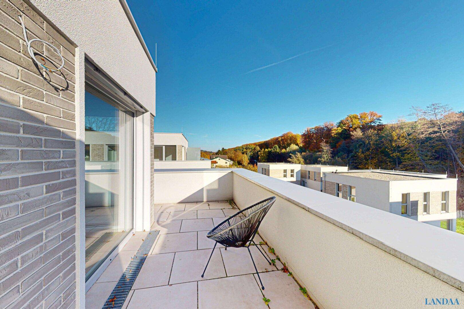 Geräumiger Balkon mit Fliesenboden und einem modernen Stuhl, bietet einen weiten Blick ins Grüne.