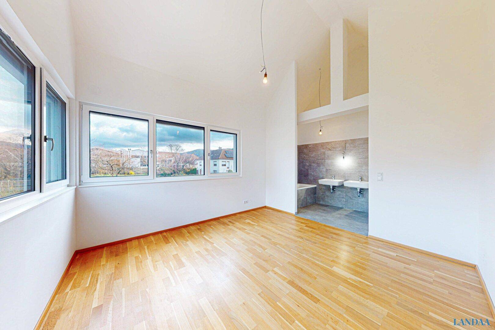 Großes Schlafzimmer mit Holzboden und offenem Zugang zu einem modernen Badezimmerbereich.