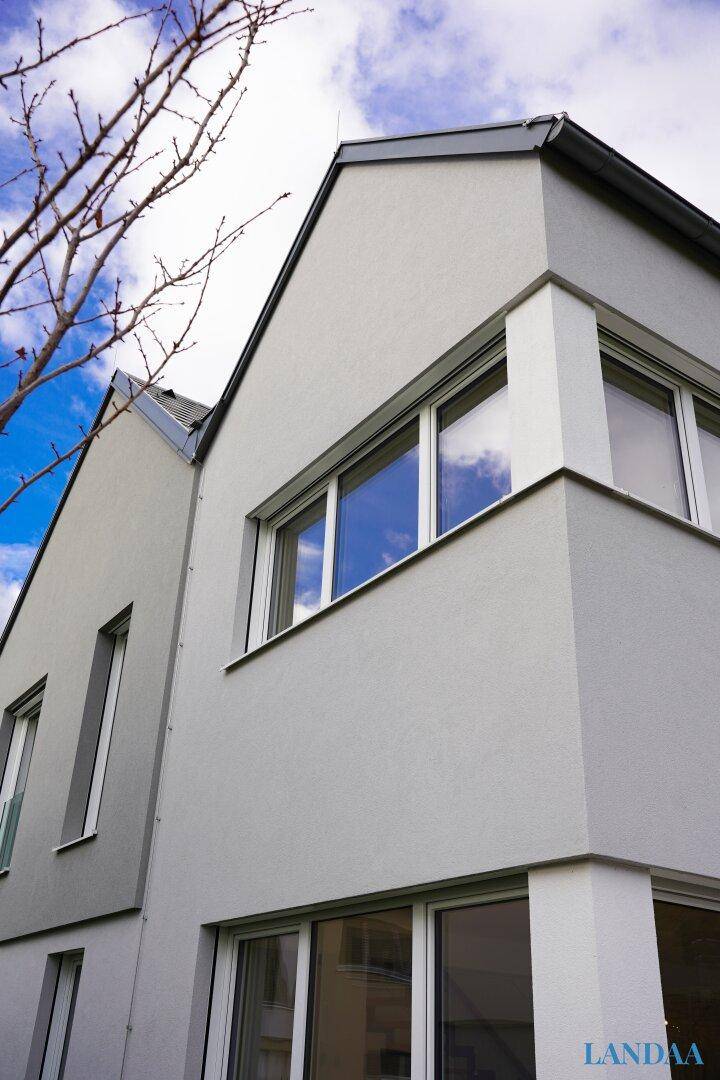 Moderne Hausfassade in hellem Grau mit großen Fenstern und klaren architektonischen Linien.