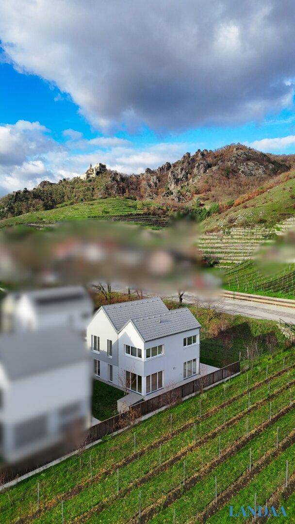 Luftaufnahme eines modernen Hauses umgeben von Weinbergen und Hügeln mit einer Burg in der Ferne.