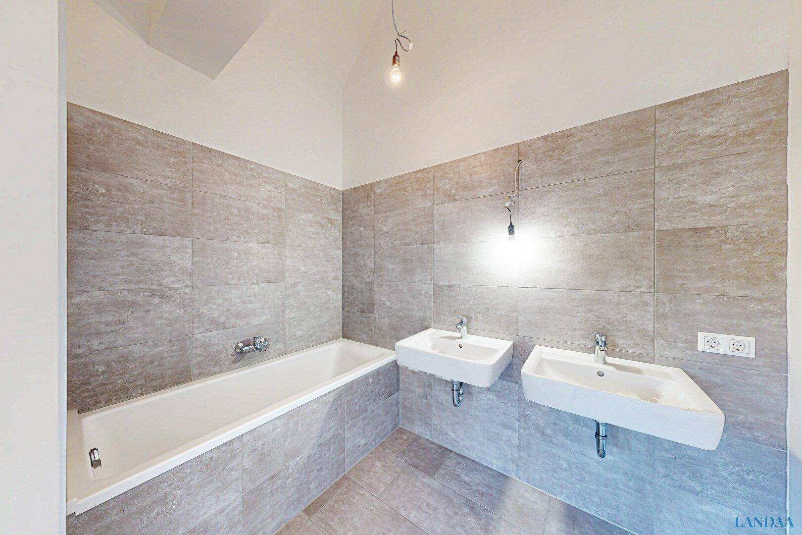 Modernes Badezimmer mit Badewanne, zwei Waschbecken und großformatigen grauen Fliesen.