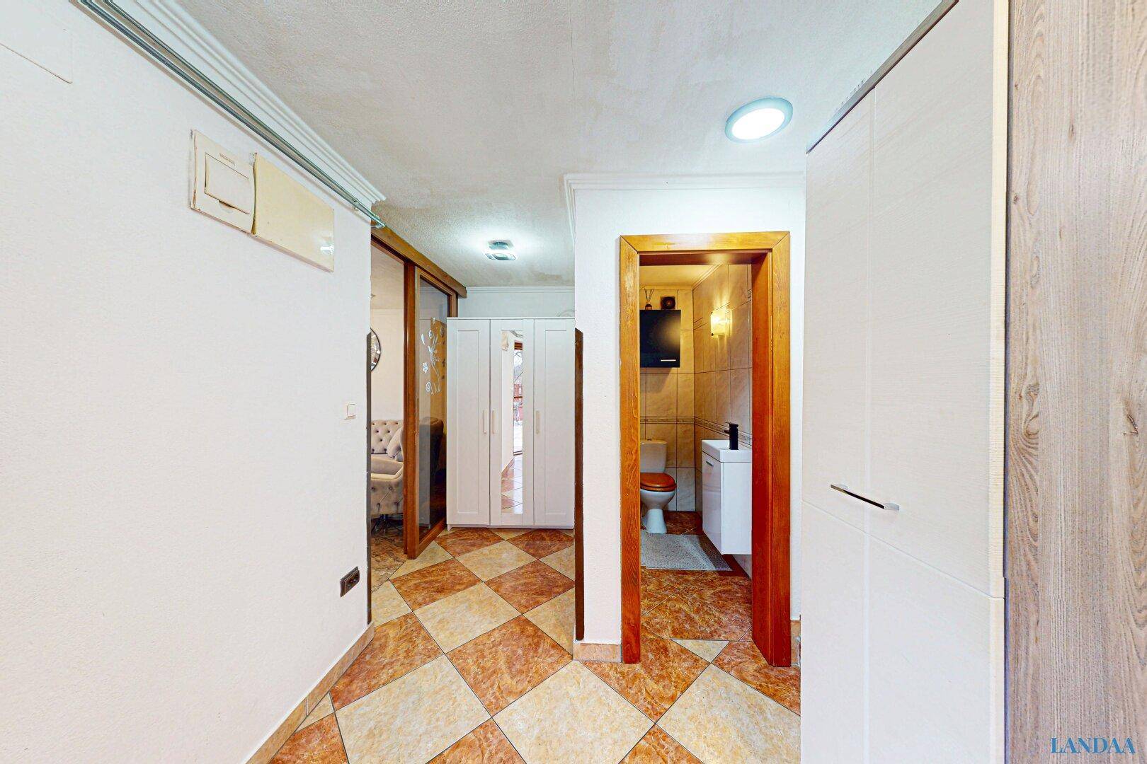 Flur mit gemustertem Fliesenboden und Zugang zu einem kleinen Badezimmer oder WC.