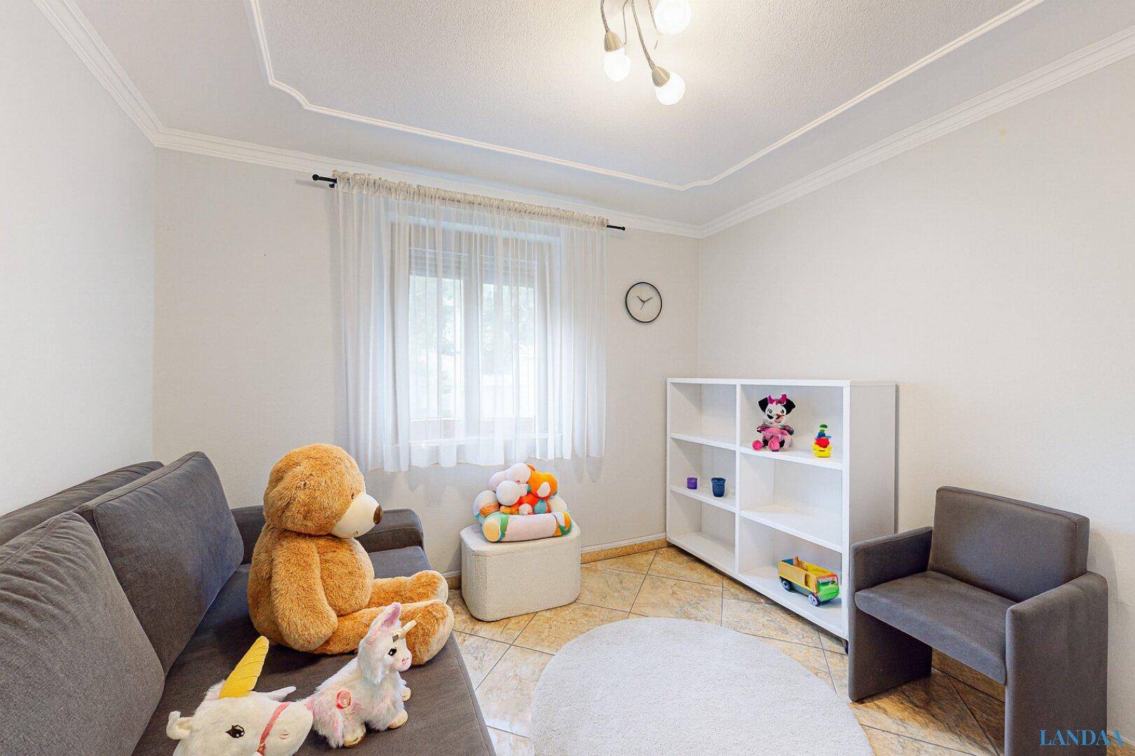 Helles Kinderzimmer oder Gästezimmer mit Spielzeug, Sofa und großem Fenster für natürliche Beleuchtung.