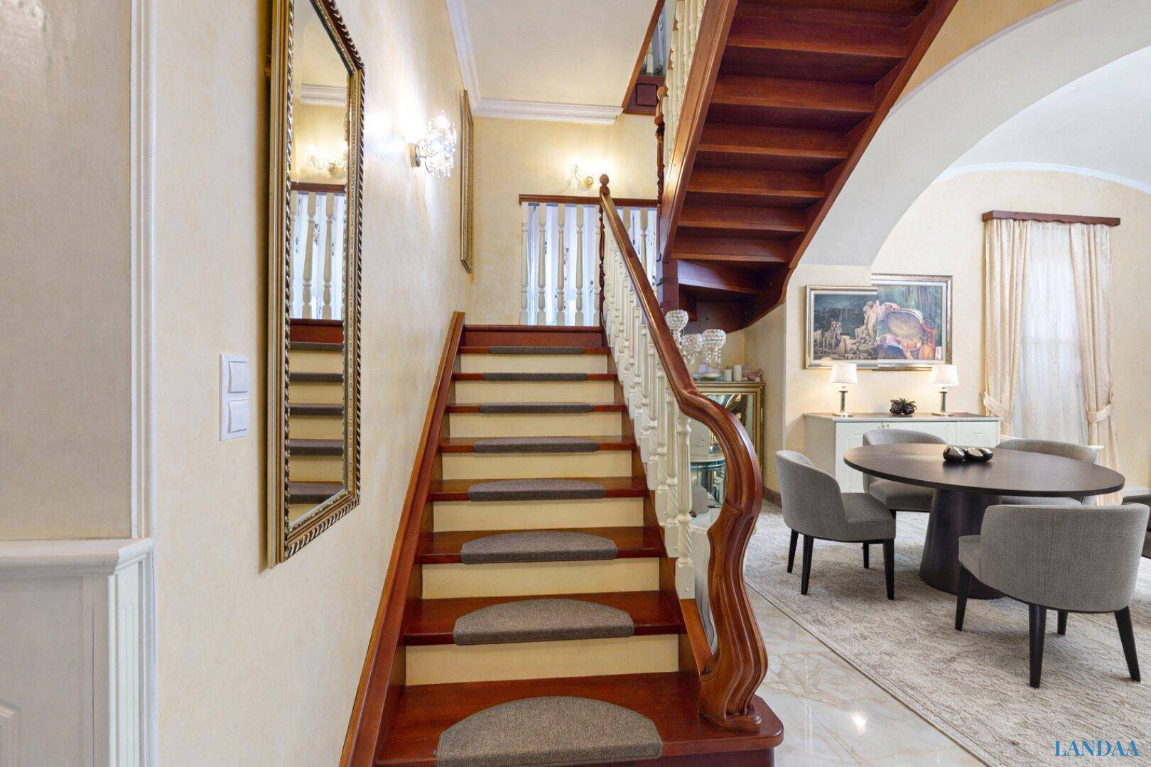 Elegantes Treppenhaus mit Holzgeländer und Marmorboden, führt zu den oberen Etagen.