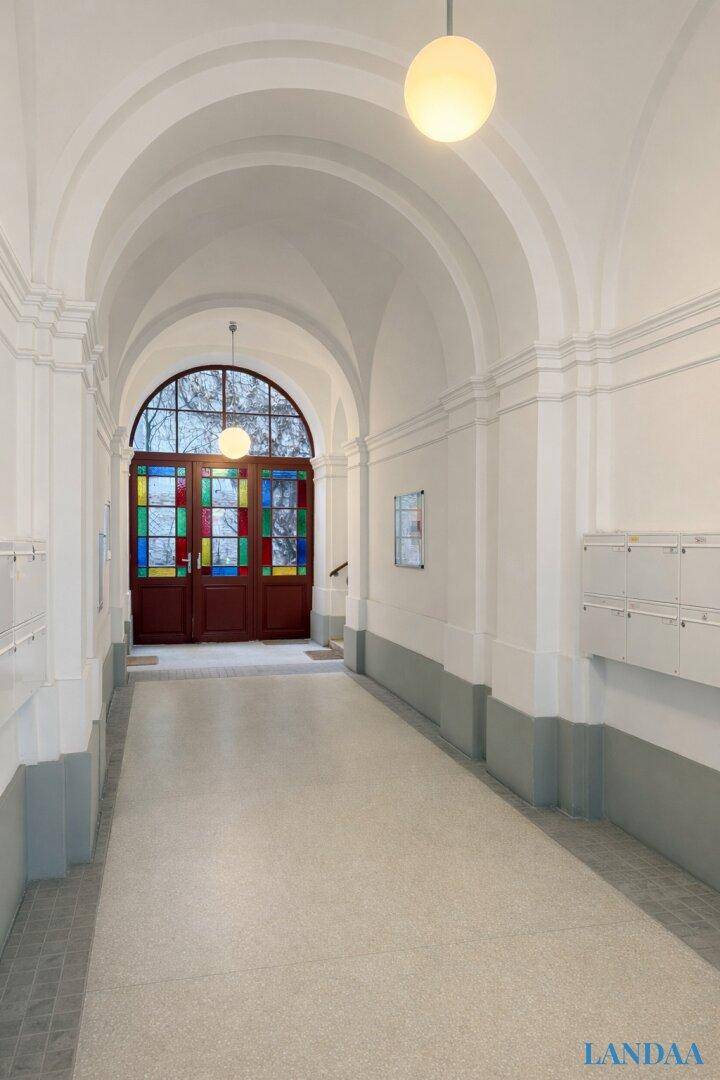 Historischer Eingangsbereich mit Gewölbedecken und farbigen Glasfenstern, führt zum Treppenhaus.