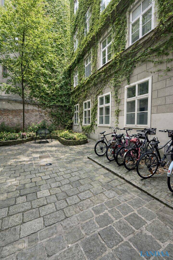 Grüner Innenhof mit Kopfsteinpflaster und Fahrradstellplätzen, umgeben von bewachsenen Fassaden.