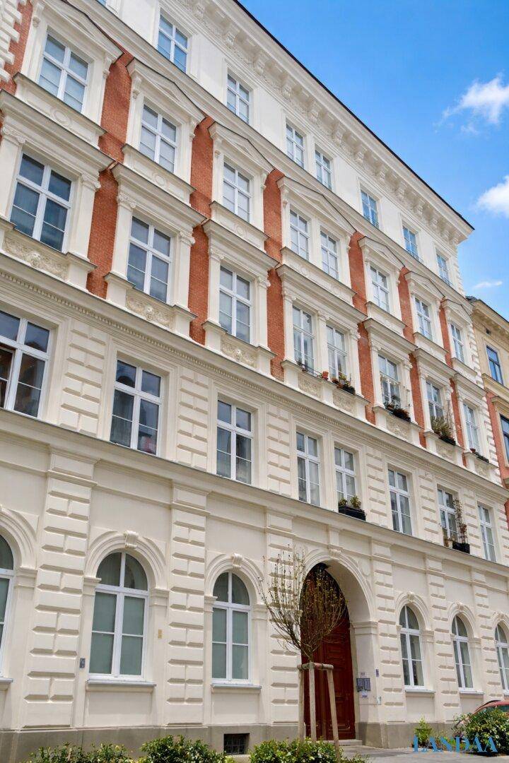 Historische Fassade eines Mehrfamilienhauses mit eleganten Details und vielen Fenstern.