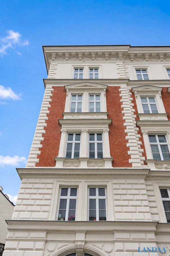 Detailansicht der oberen Etagen einer historischen Fassade mit roten Ziegelakzenten und Stuckverzierungen.
