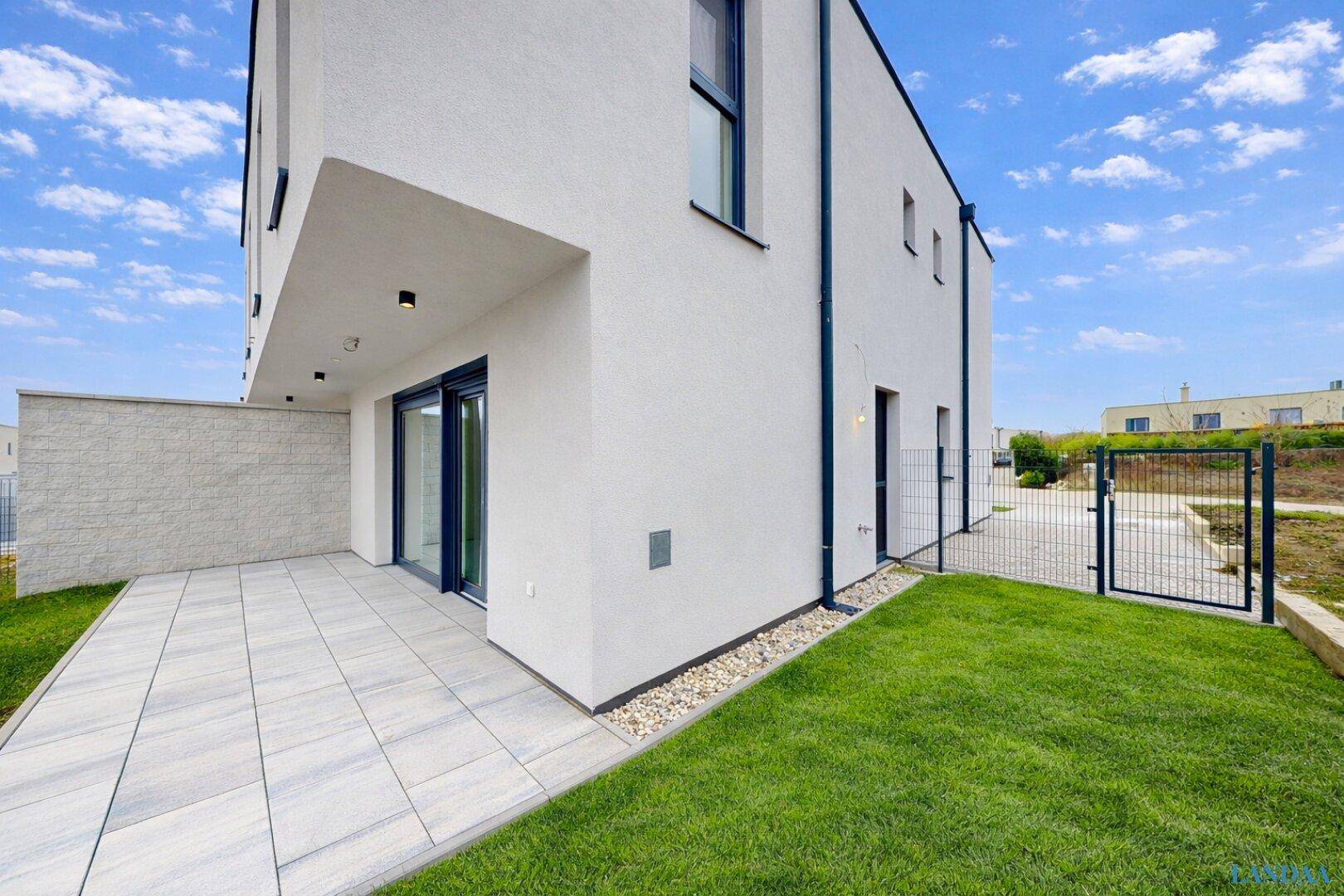 Seitenansicht des modernen Hauses mit gepflasterter Terrasse und Rasenfläche.