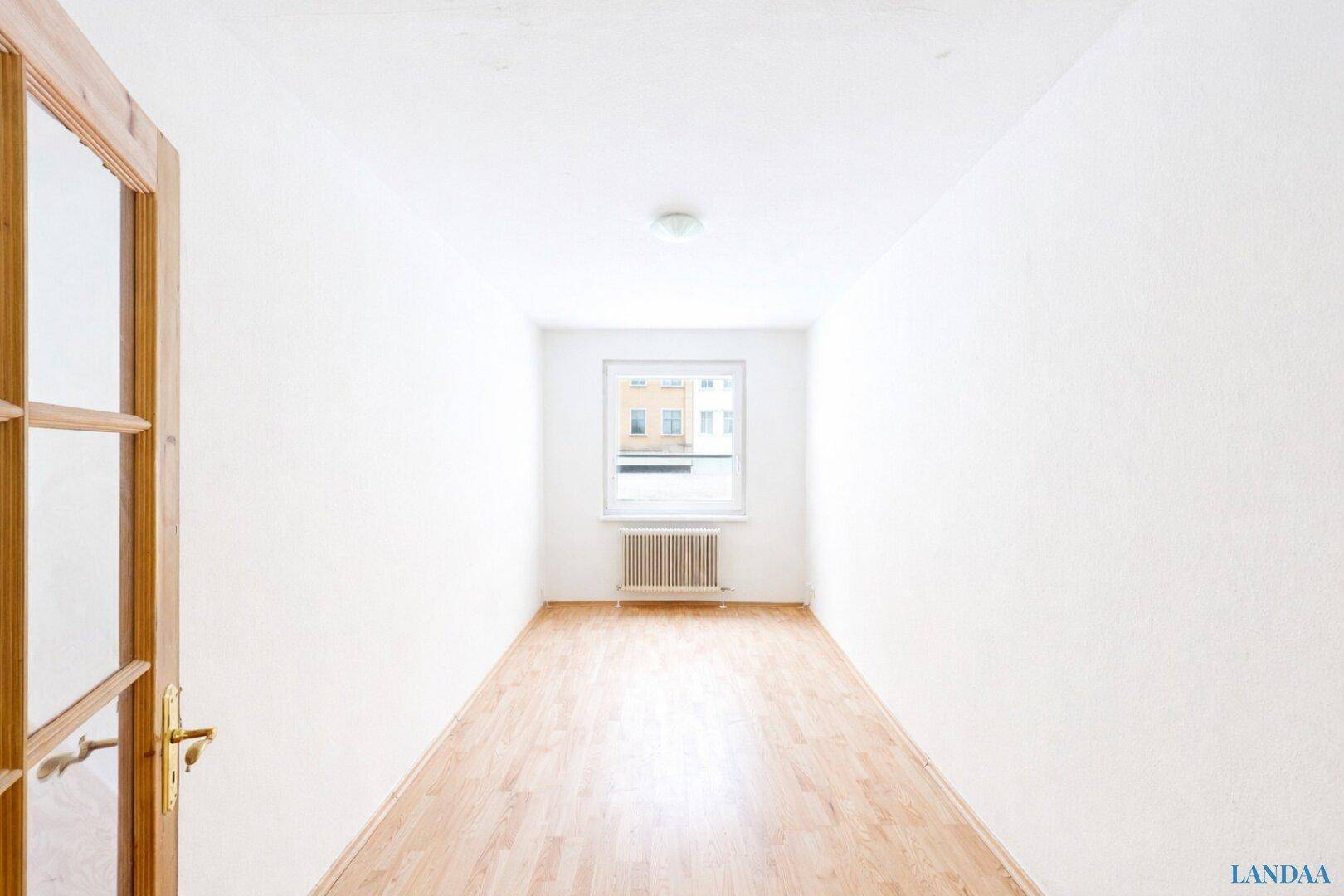 Heller, leerer Raum mit Parkettboden und einem Fenster, das den Blick nach draußen freigibt.