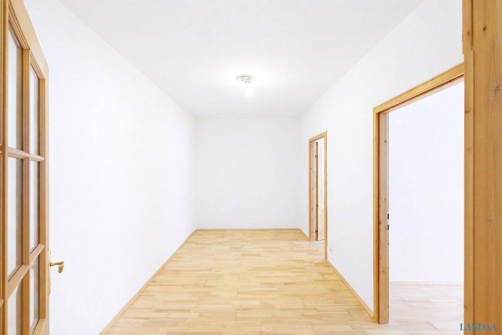 Leerer Flur mit hellem Parkettboden und mehreren Holztüren.