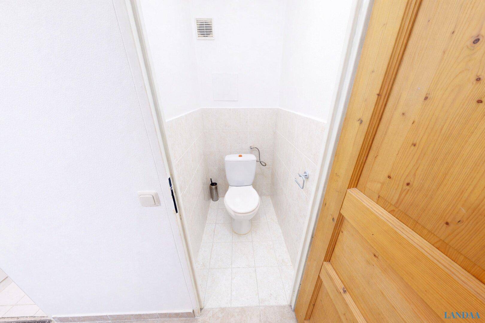 Kleines Gäste-WC mit weißer Toilette und hellen Fliesen an Wänden und Boden.