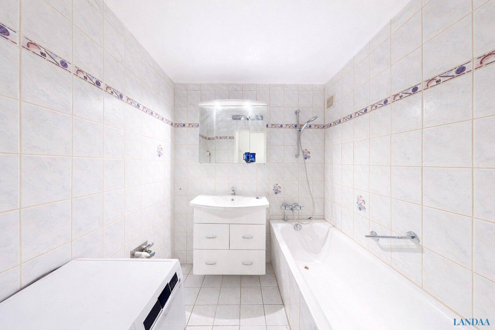 Helles Badezimmer mit Badewanne, Waschbecken und weißen Fliesen an Wänden und Boden.