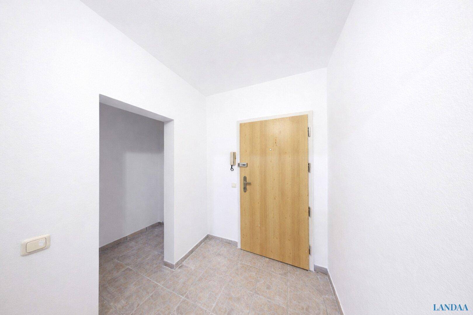 Eingangsbereich mit Fliesenboden und einer Holztür, die in die Wohnung führt.