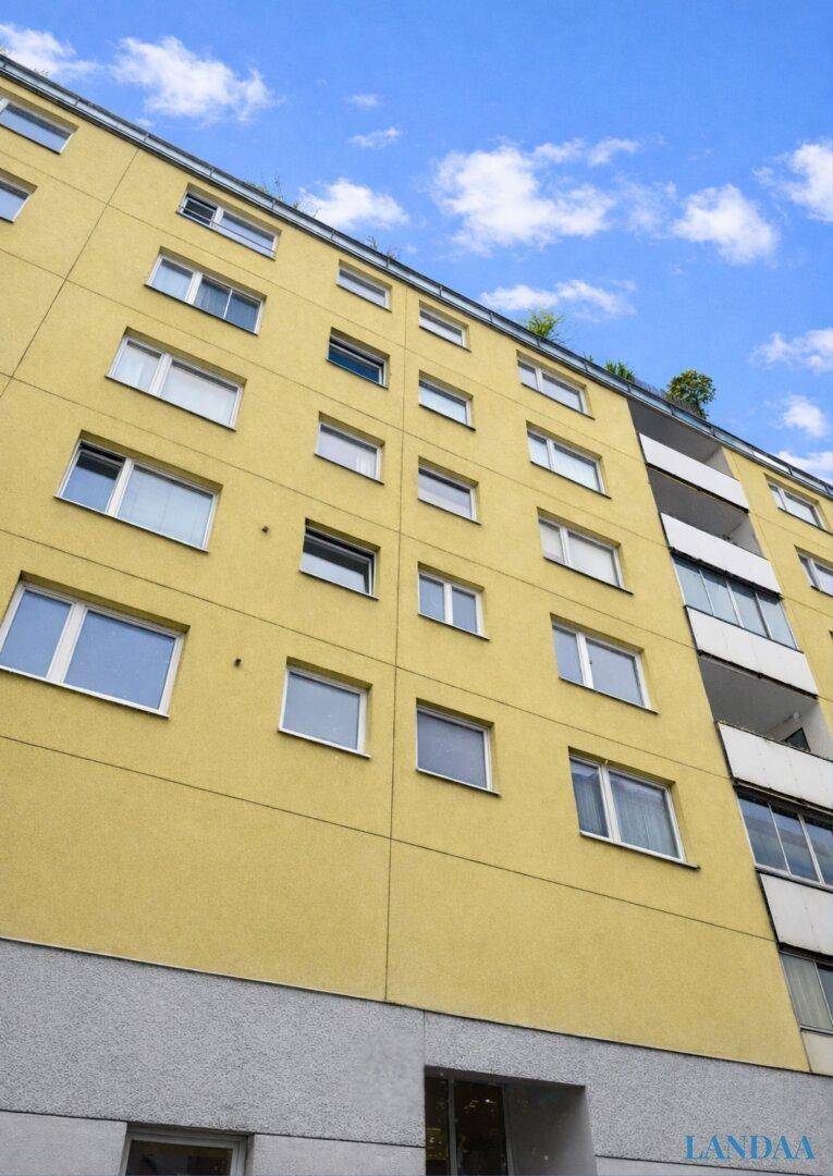 Gelbe Fassade eines Mehrfamilienhauses mit vielen Fenstern und Balkonen unter blauem Himmel.