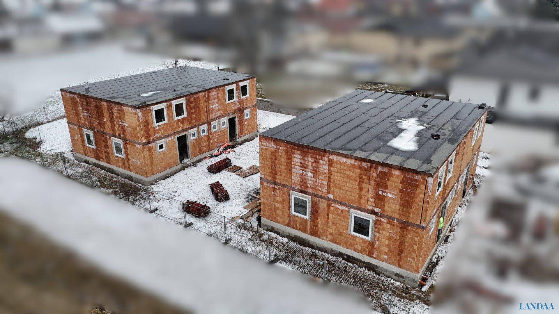 Luftaufnahme von zwei Rohbauten mit Ziegelwänden und flachen Dächern, umgeben von Schnee.