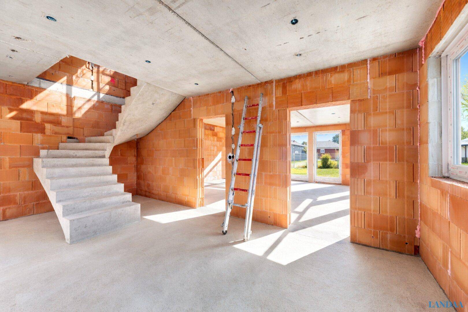 Geräumiger Innenraum im Rohbau mit Ziegelwänden, Betonboden und einer Betontreppe.