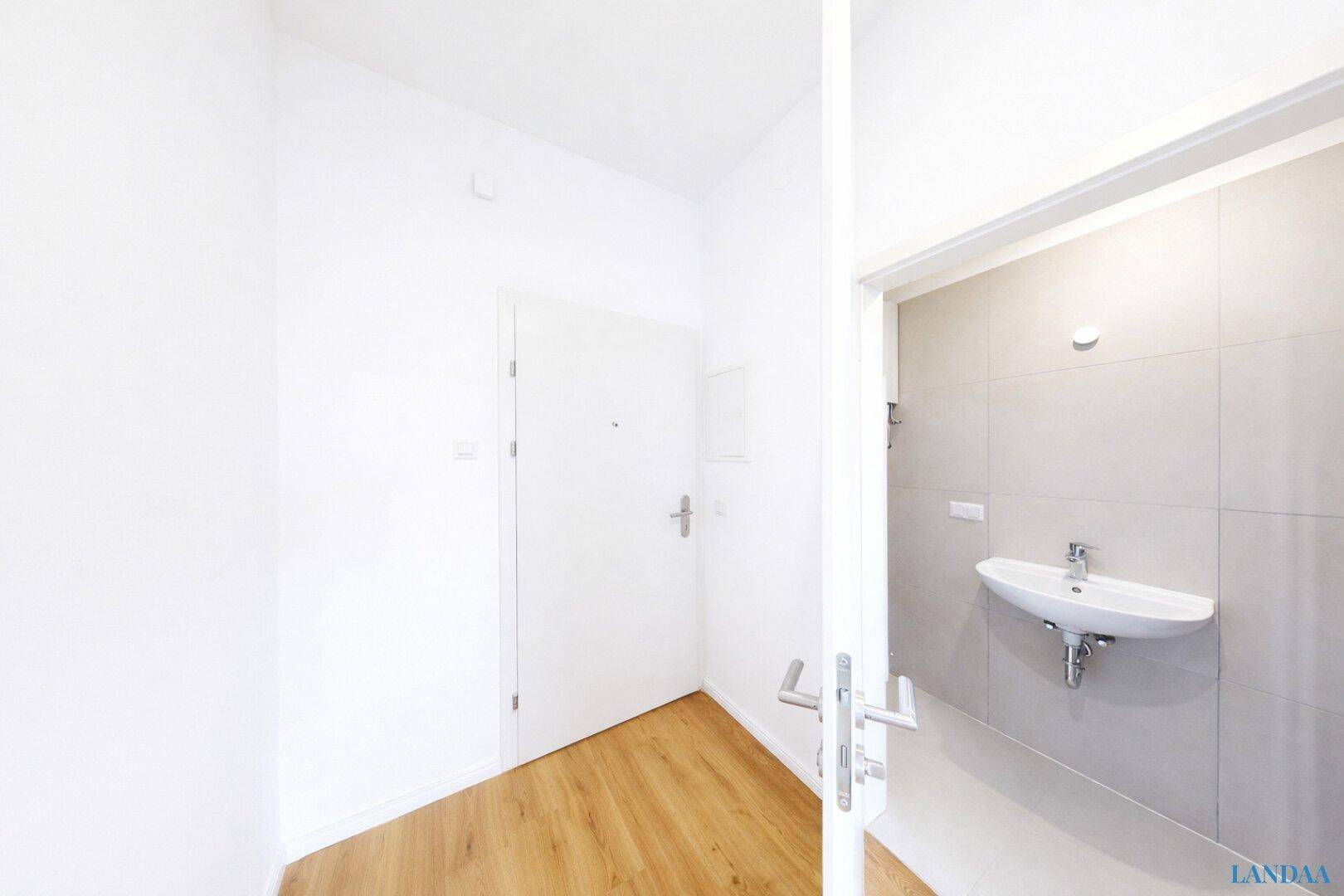 Heller Eingangsbereich mit Holzfußboden und Zugang zu einem modernen Badezimmer.