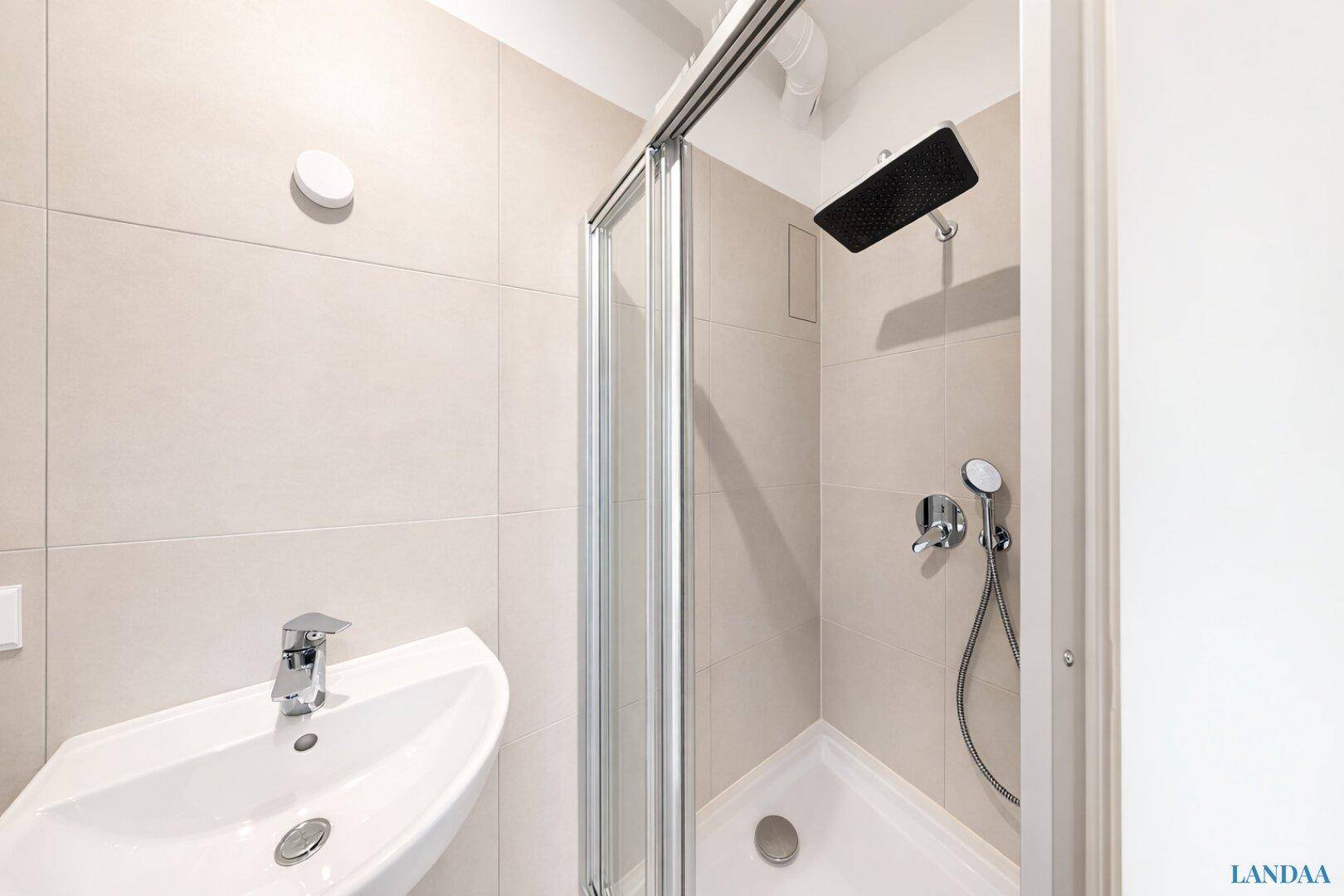 Modernes Badezimmer mit Duschkabine, Waschbecken und hellen Fliesen.