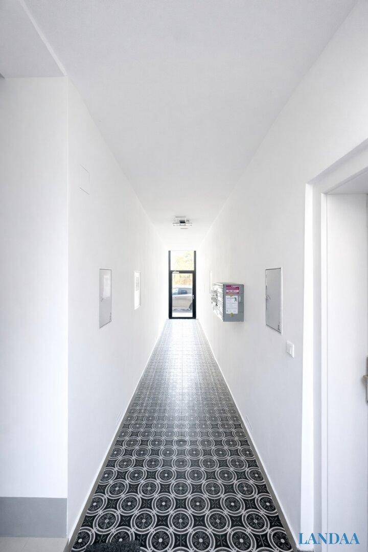 Langer, heller Hausflur mit auffälligem Fliesenboden und Eingangstür am Ende.