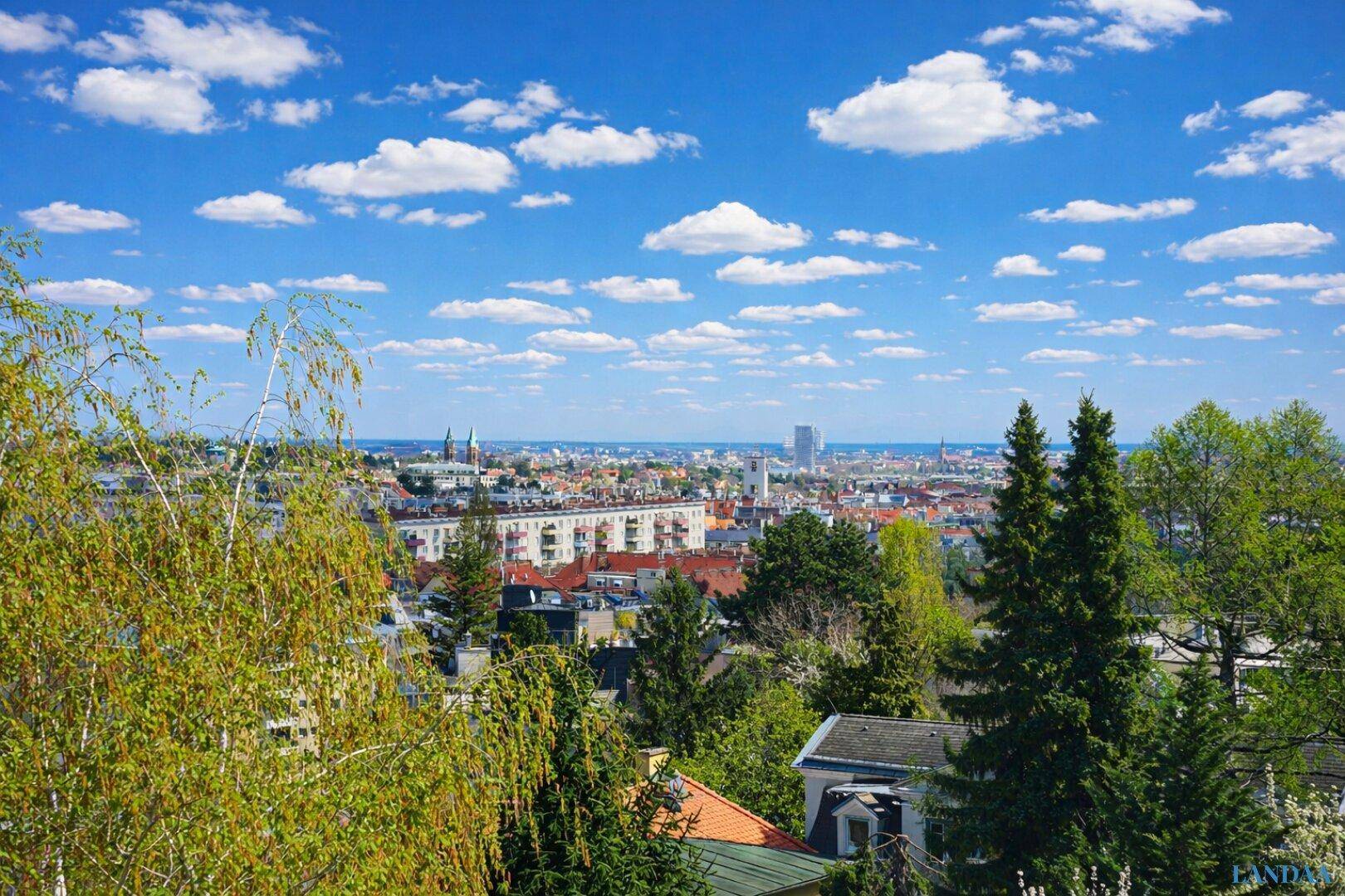 Panoramablick über die Stadt mit grünen Hügeln und blauem Himmel.
