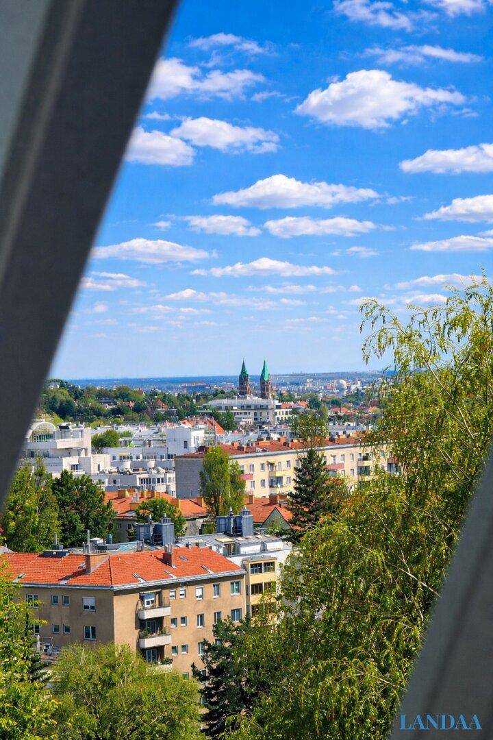 Blick aus dem Fenster auf die Stadt mit historischen Gebäuden und grünen Bäumen.