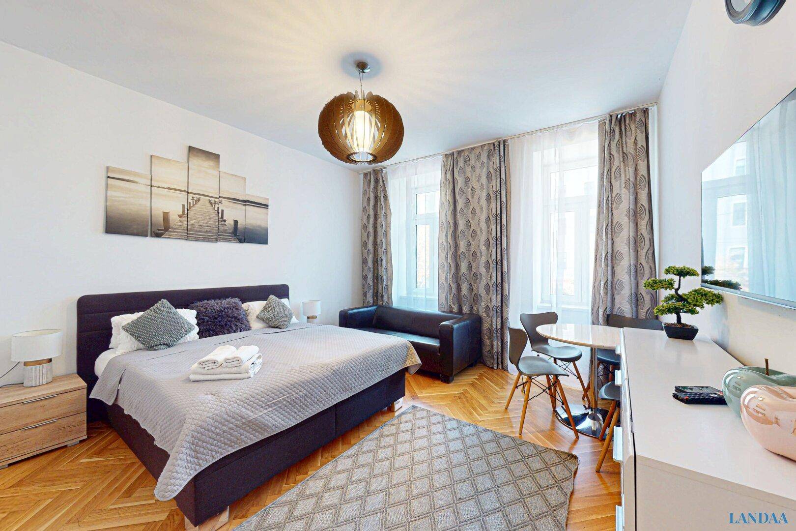 Gemütliches Schlafzimmer mit Doppelbett, Parkettboden und kleiner Sitzecke.