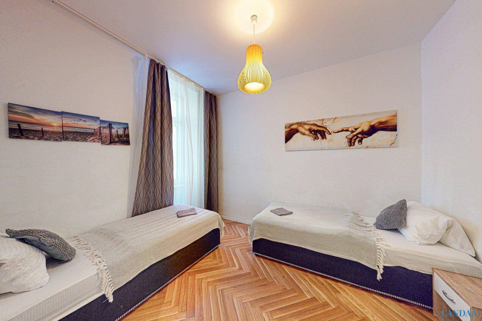 Schlafzimmer mit zwei Einzelbetten, Parkettboden und Kunstwerken an der Wand.