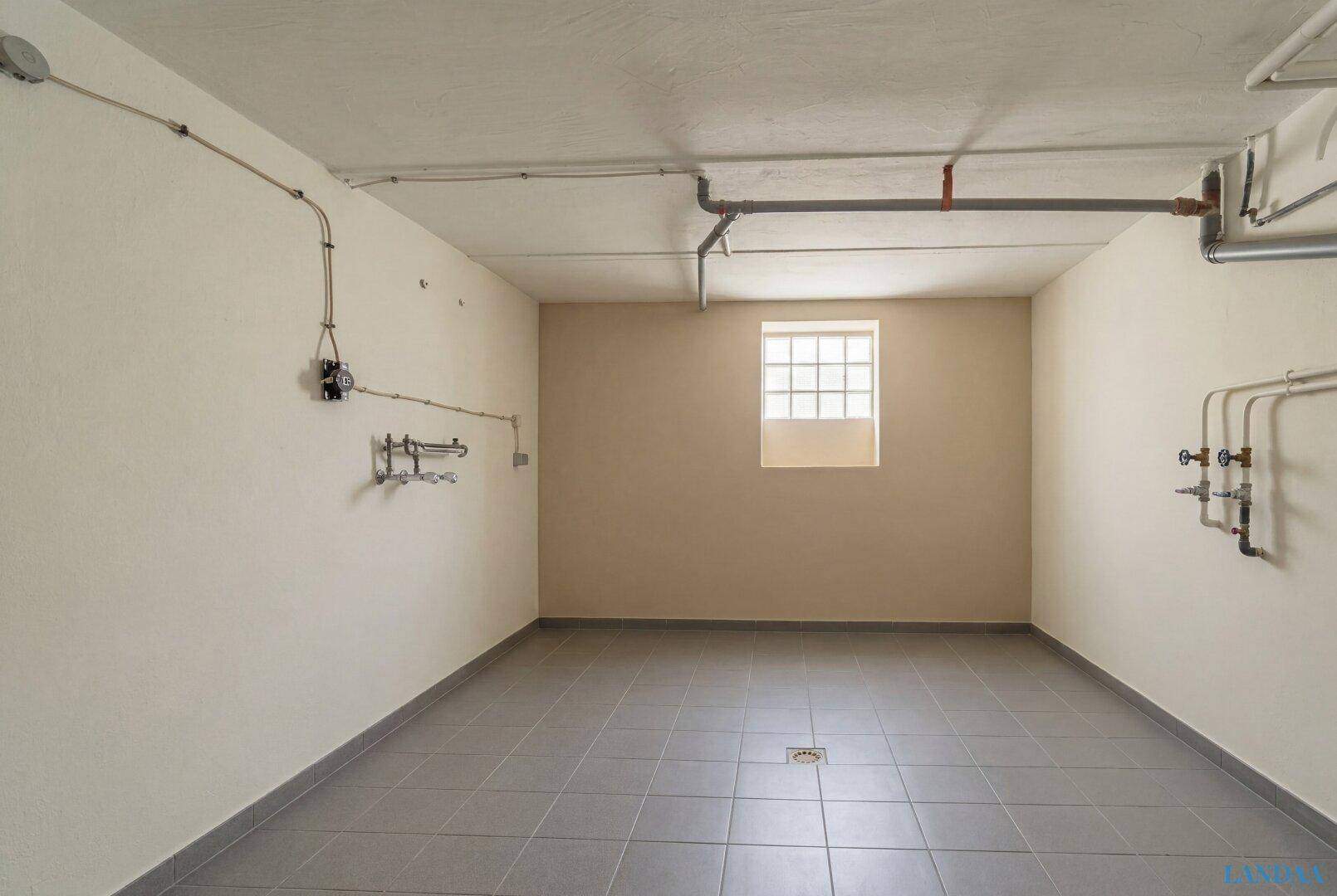 Funktionaler Hauswirtschaftsraum im Keller mit Fliesenboden und sichtbaren Installationen.