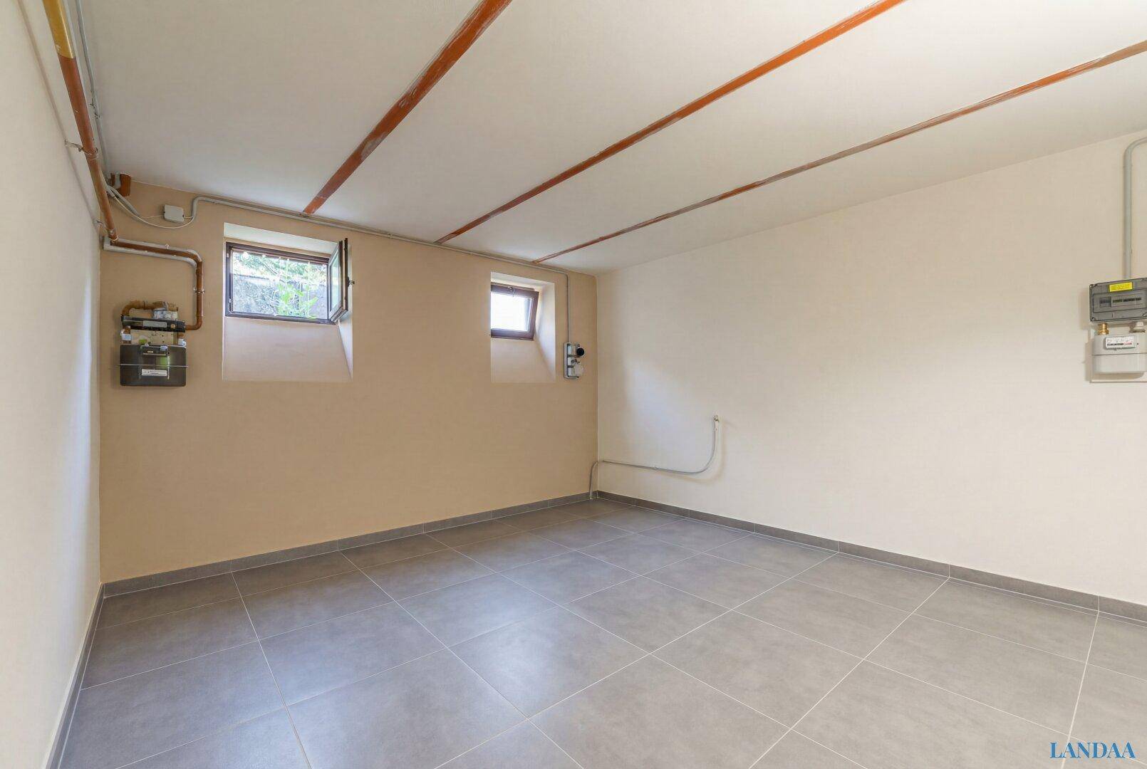 Heller Kellerraum mit Fliesenboden, kleinen Fenstern und Zählerinstallationen an der Wand.