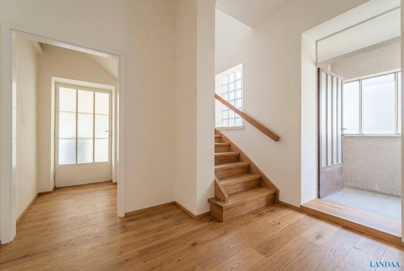 Freundlicher Eingangsbereich mit Holztreppe, Holzboden und Zugang zu einem kleinen Balkon.
