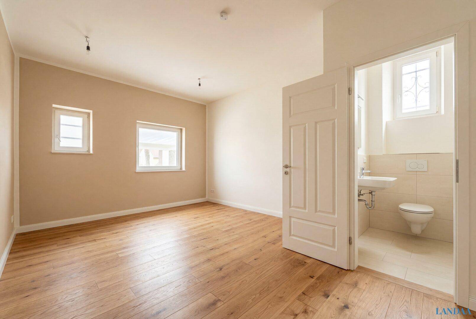 Schlafzimmer mit Holzboden und direktem Zugang zu einem modernen Badezimmer mit Fenster.